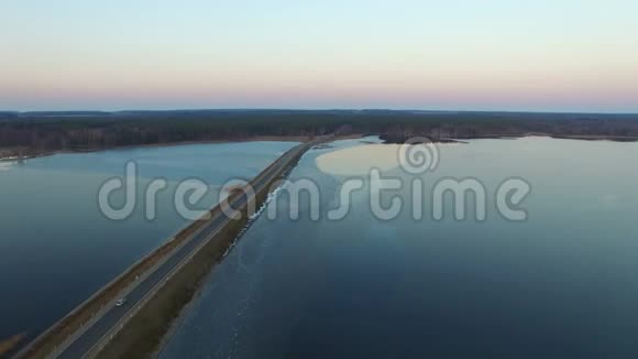 4K日落时飞越冰冻湖上的道路鸟瞰视频的预览图