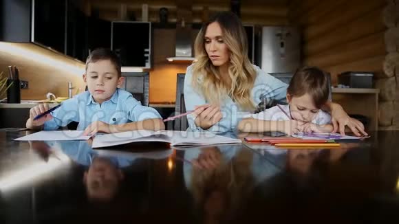 两个孩子的幸福家庭母亲帮助儿子们坐在厨房的大桌子旁做作业视频的预览图