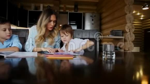 两个孩子的幸福家庭母亲帮助儿子们坐在厨房的大桌子旁做作业视频的预览图