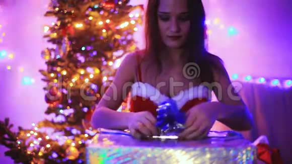 年轻快乐的女人打开神奇的圣诞礼物与魔术发光的灯女孩坐在圣诞树旁边视频的预览图