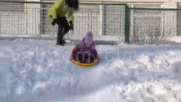 儿童骑在山上的盘子里儿童在冬天雪橇视频的预览图