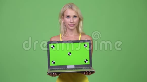 年轻快乐的金发女郎带着绿色背景的笔记本电脑视频的预览图