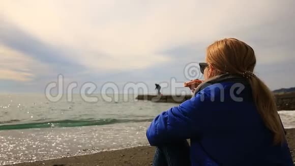 天气不好一个女人独自坐在荒无人烟的海滩上看着大海吃披萨视频的预览图