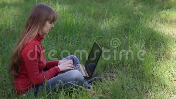 女人在电脑上打字坐在草地上视频的预览图