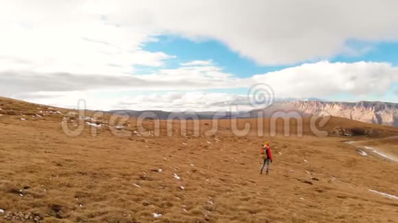 空中景色带着相机戴着帽子的女孩旅行者带着背包和太阳镜带着黄色的草走在斜坡上视频的预览图