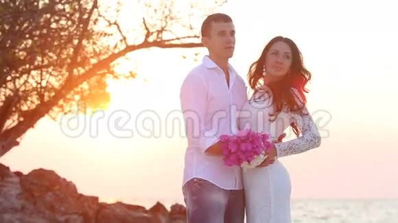 新娘和新郎在日出的沙滩上拥抱和欢笑视频的预览图