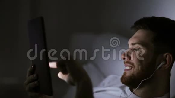 晚上床上有平板电脑和耳机的男人视频的预览图