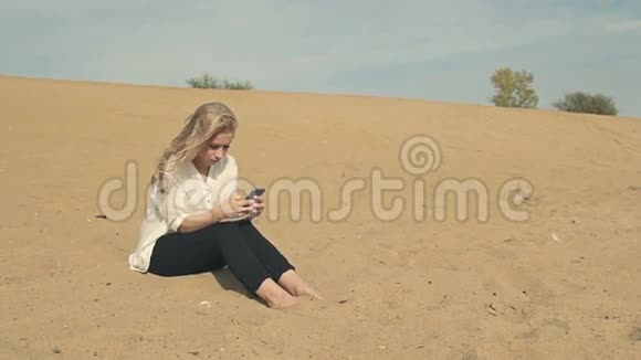 光脚女孩拿着电话坐在沙滩上视频的预览图