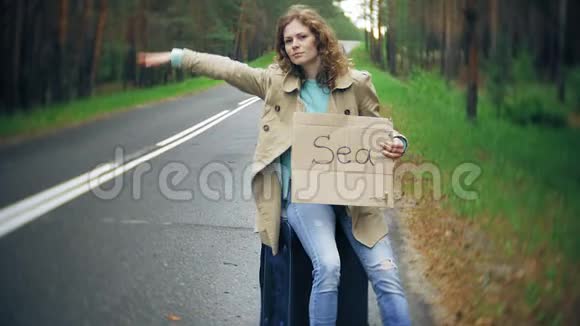 年轻漂亮的女人站在路上一个手提箱放在桌子上上面写着大海视频的预览图