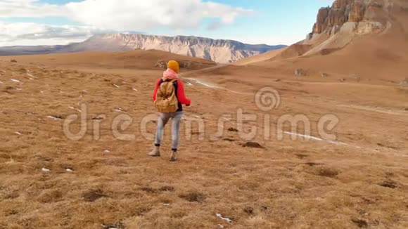 空中景色带着相机戴着帽子的女孩旅行者带着背包和太阳镜带着黄色的草走在斜坡上视频的预览图