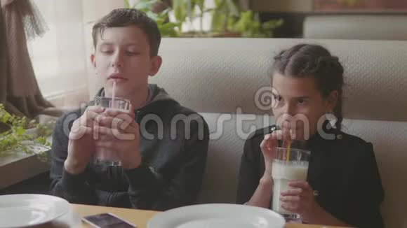 两个可爱的孩子一起喝奶昔或调味饮料室内慢动作视频咖啡馆快餐男孩和女孩视频的预览图