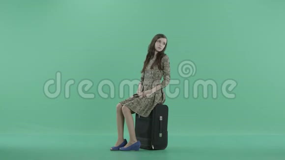 一个年轻的女人坐在黑色的行李上等待着视频的预览图