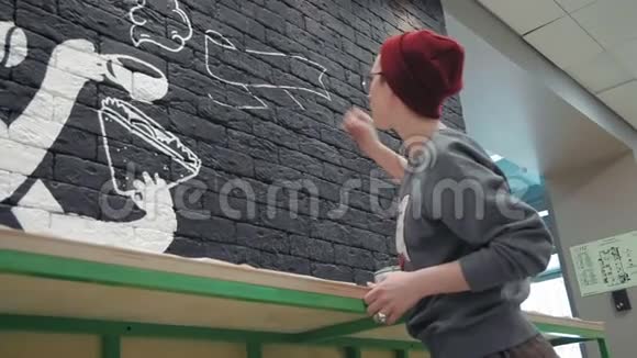 年轻的女画家在咖啡店的黑砖墙上做白色设计视频的预览图