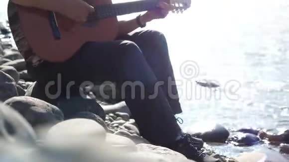 阳光明媚的日子戴墨镜的家伙坐在山河边弹吉他3840x2160视频的预览图
