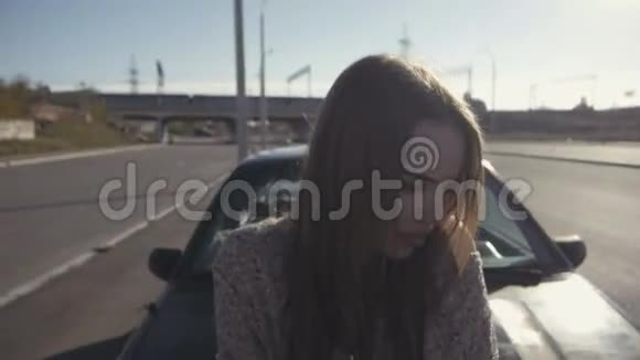 金发女人盯着镜头低头坐在车罩上视频的预览图