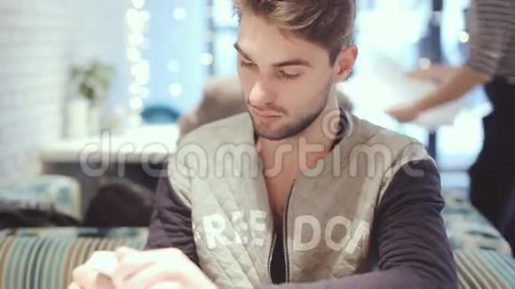 有智能手机的年轻人坐在咖啡馆里特写视频的预览图