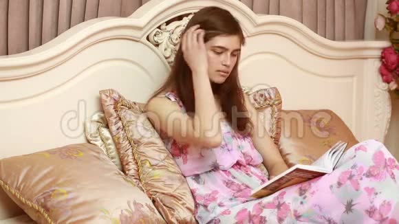 年轻迷人的美女女孩读一本书躺在酒店房间的豪华床上一个年轻女孩的卧室视频的预览图