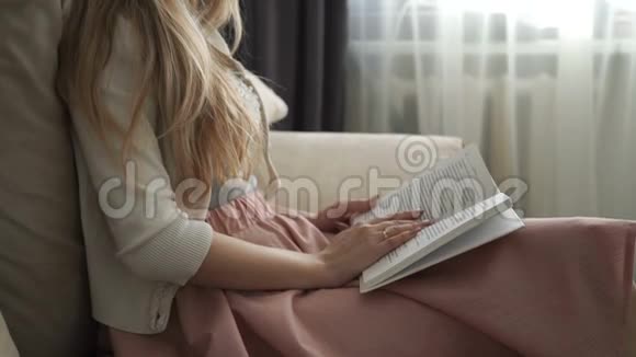 美丽的年轻女子坐在沙发上看书微笑着视频的预览图