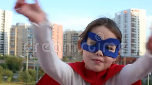 在城市背景下穿红色斗篷的超级英雄女孩视频的预览图