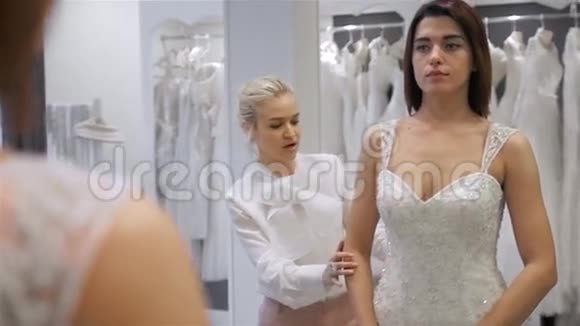 漂亮的年轻女人正在商店里挑选婚纱店员正在帮助她女童群体视频的预览图