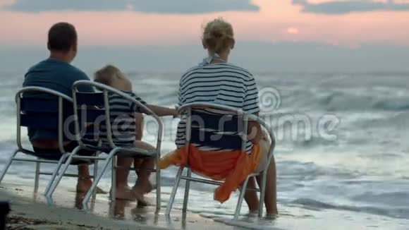 日落时分一家三口坐在海边的椅子上视频的预览图