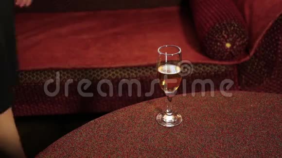 穿着黑色连衣裙的女人腿穿过沙发把一杯香槟放在桌子上视频的预览图