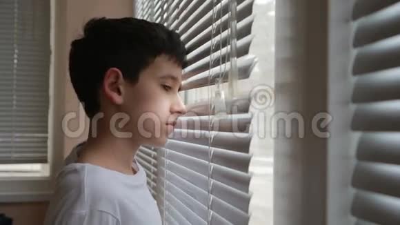 男孩从窗户透过百叶窗看着街道视频的预览图