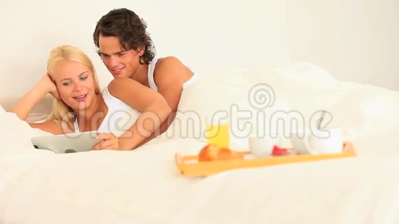 一对幸福的夫妻在床上一起吃早餐和平板电脑视频的预览图