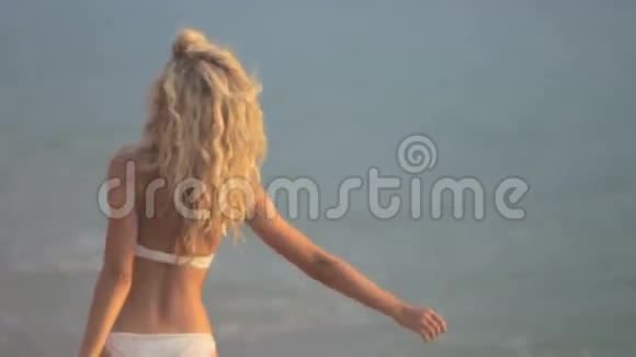 日落时年轻漂亮的女孩沿着海滩散步视频的预览图