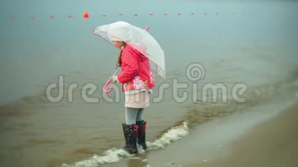 小美丽的女孩带着雨伞在雨中玩耍沿着海岸散步视频的预览图