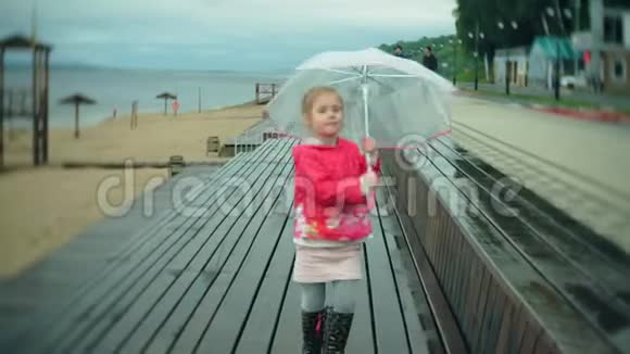 小美丽的女孩带着雨伞在雨中玩耍沿着海岸散步视频的预览图