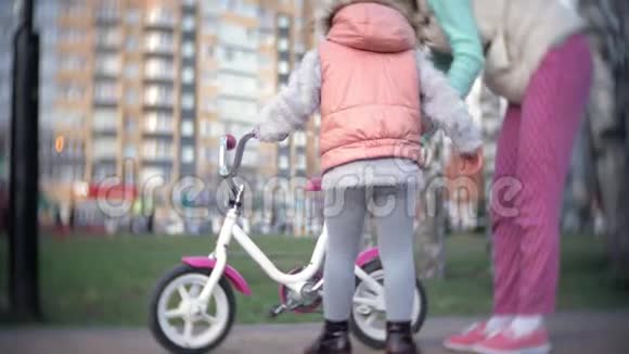 在温暖的春天里一位笑着的母亲把她的女儿推到前面她教她骑自行车视频的预览图