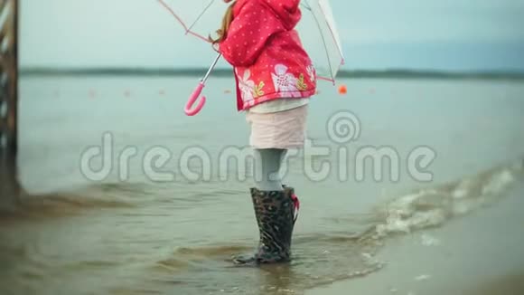 小美丽的女孩带着雨伞在雨中玩耍沿着海岸散步视频的预览图