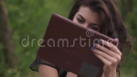 夏天在木墩上坐着时一位美丽的黑发女人在数码平板电脑上玩耍她的脸上洋溢着激动的表情视频的预览图