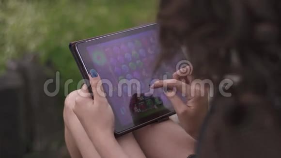 在数码平板电脑上玩游戏的迷人黑发女人的后视图绿草背景视频的预览图