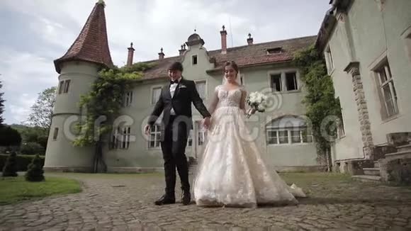 新婚夫妇正在大城堡附近的公园里散步美丽的新娘英俊的新郎视频的预览图