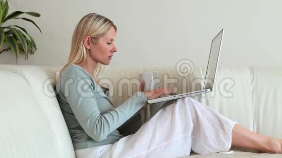 女人在喝咖啡膝盖上放着笔记本电脑视频的预览图