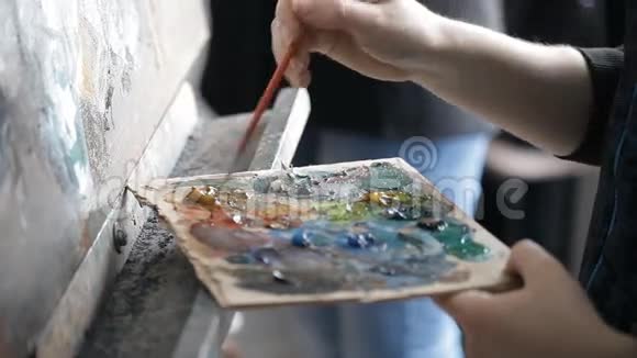 画家把画笔放到画架上的颜料调色板上视频的预览图