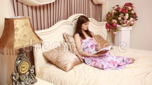 年轻迷人的美女女孩读一本书躺在酒店房间的豪华床上一个年轻女孩的卧室视频的预览图