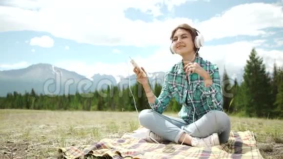 休闲的女孩听着音乐坐着在夕阳下的绿色田野里放松视频的预览图