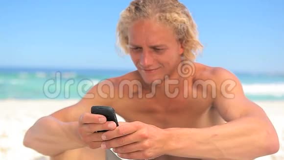 微笑的金发男人坐在沙滩上发短信视频的预览图