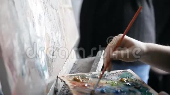 画家把画笔放到画架上的颜料调色板上视频的预览图