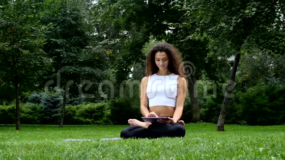 在公园做平板电脑的年轻女子瑜伽视频的预览图