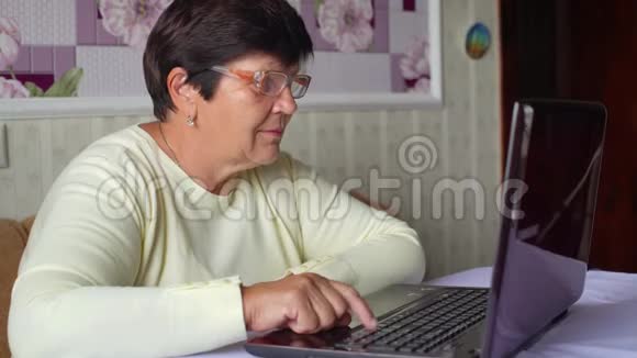 戴眼镜的老年妇女在家里用笔记本电脑上网视频的预览图