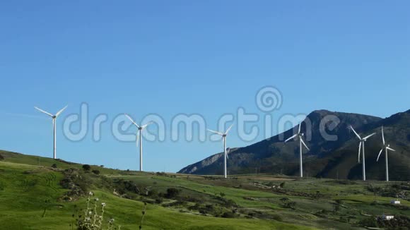 风力涡轮机在阳光明媚的日子里能量在田野道路和山脉一起移动视频的预览图