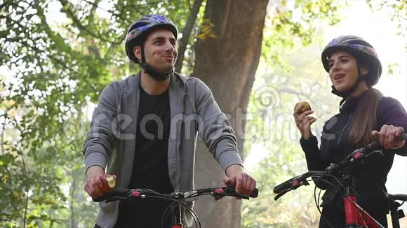 漂亮的夫妇在秋天的公园里骑自行车散步慢动作视频的预览图