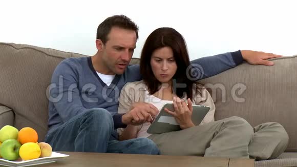 可爱的一对夫妇坐在沙发上用电脑平板电脑视频的预览图