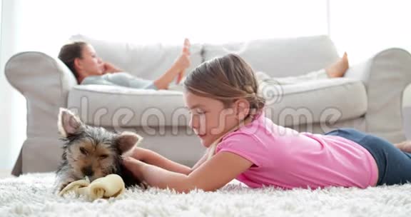 小女孩玩小狗嚼骨头妈妈在沙发上看书视频的预览图