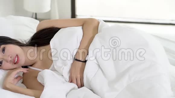美丽的亚洲年轻女子躺在床上头靠在枕头上舒适而快乐地移动着全景相机放松的女孩视频的预览图