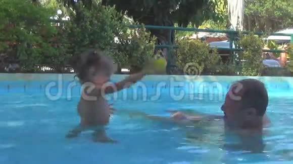在游泳池里一个漂亮的婴儿向爷爷扔了一个黄色的球水喷雾在一个人面前飞舞他拧你视频的预览图